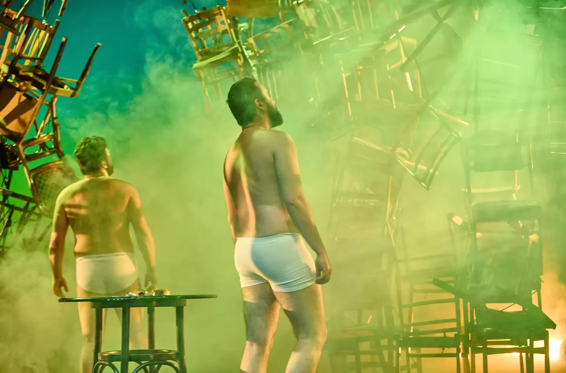 Medium shot of two actors, in underwear, looking up into the smoky background with their backs towards the camera