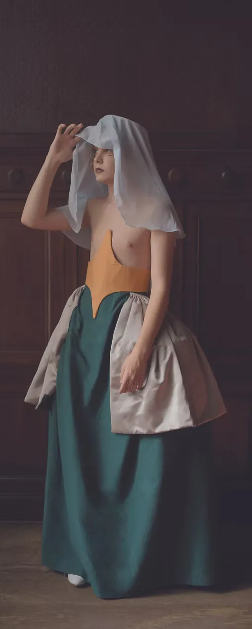 A figure in a teal skirt and amber bodice wears a wide white apron-veil draped over the head and face, one hand lifting its edge. The composition quotes Dutch Golden Age devotional imagery, reframing the overlooked figures of history as subjects worthy of study.
