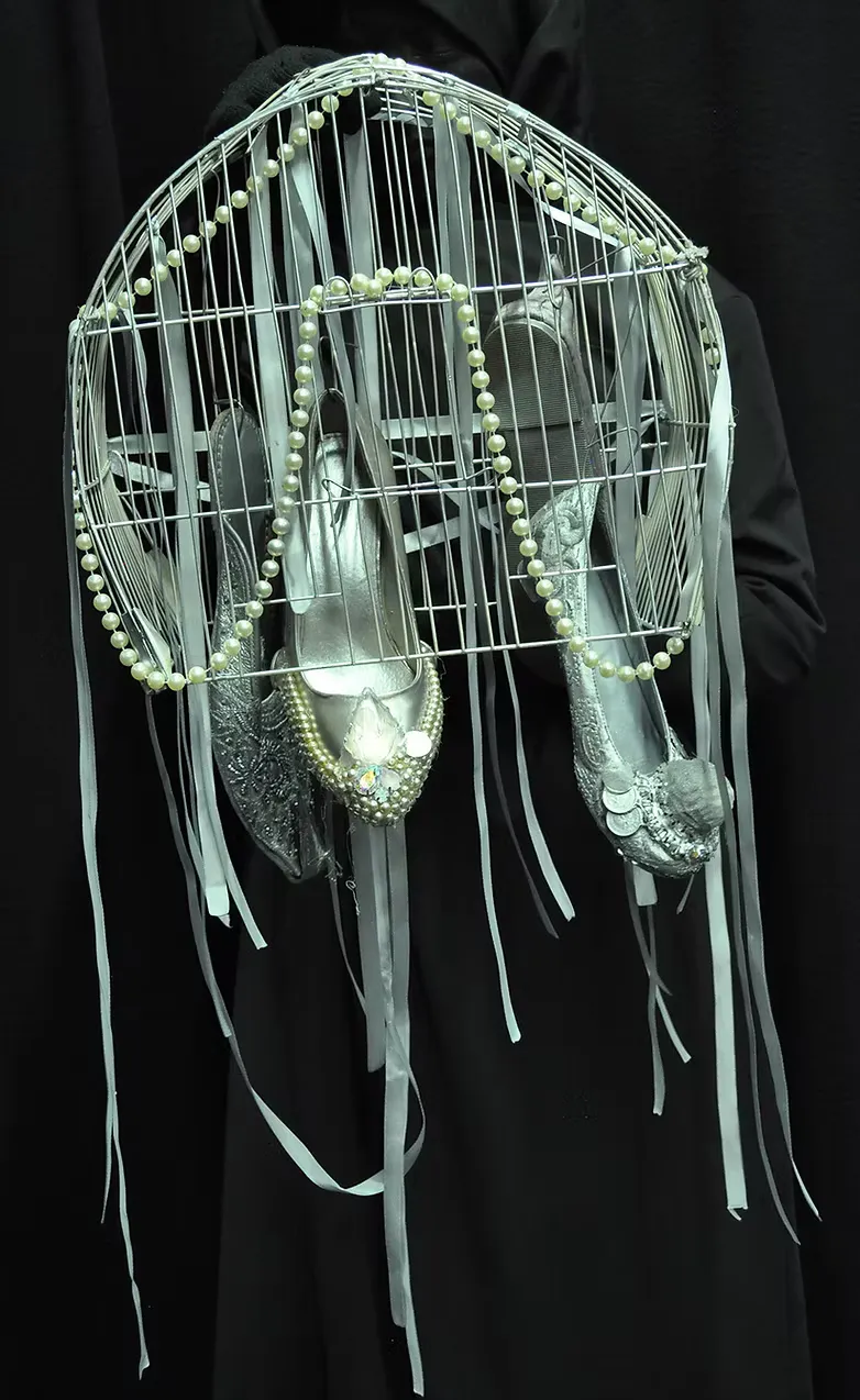 A delicate dome-shaped structure built from white wire hoops, adorned with pearl strands, pale ribbons, and small feathers. Craft materials transformed into something fragile and otherworldly.